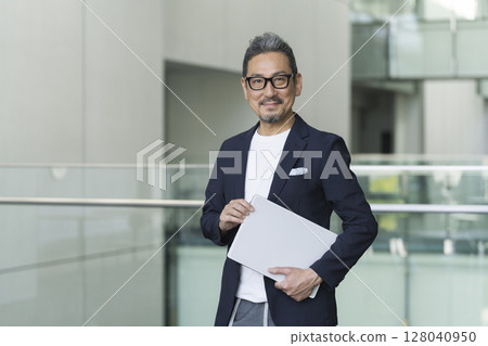 Smiling senior businessman looking at the camera with a laptop 128040950