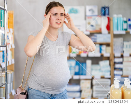 Pregnant woman having headache in drugstore 128041294