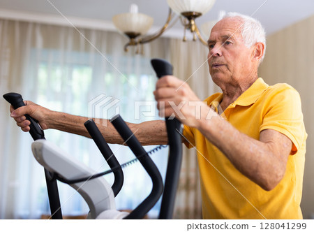 Senior man training on cross-trainer at home 128041299