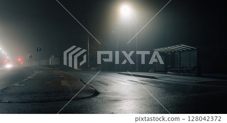 Urban night scene with a misty bus stop and glowing streetlights. 128042372