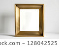 Elegant golden picture frame standing on white tabletop. Minimalistic design and neutral background 128042525