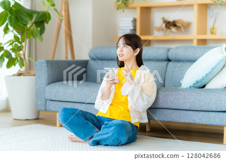 在房間裡操作智慧型手機的年輕女子 在房間裡操作智慧型手機的年輕女子 128042686