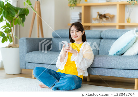 A young woman operating a smartphone in a room 128042704