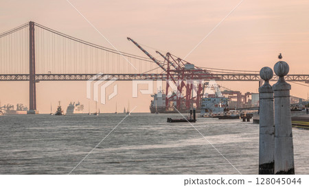 Cais das Colunas near Cais do Sodre timelapse with 25 April Bridge and cargo port terminal. Lisbon, Portugal 128045044