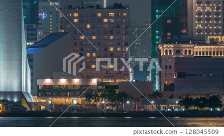 People sitting on the stairs near Hong Kong Cultural Centre with palms and towers on background timelapse. 128045509