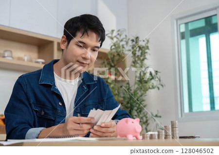 Budgeting and Savings. Young man reviewing financial documents with piggy bank. 128046502