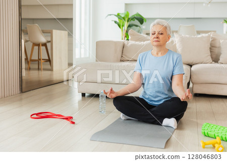 Yoga mindfulness meditation. Senior adult mature woman practicing yoga at home. Mid age old lady sitting in lotus pose on yoga mat meditating relaxing. Older middle aged woman doing breathing practice 128046803