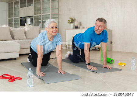 Fitness workout training. Senior adult mature healthy fit couple doing sports exercise on yoga mat on floor at home. Mid age old husband wife have training workout. Health care healthy lifestyle 128046847