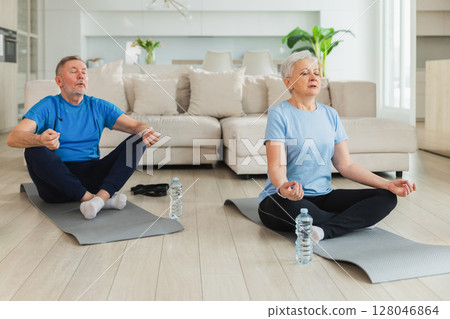 Yoga mindfulness meditation. Senior adult mature couple practicing yoga at home. Mid age old husband wife sitting in lotus pose on yoga mat meditating relaxing. Family doing breathing practice 128046864