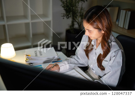 Late Night Focus. A woman diligently working on documents in a quiet office. Late Night Focus. A woman diligently working on documents in a quiet office. 128047337
