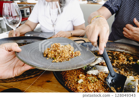 serving seafood rice from a paella pan serving seafood rice from a paella pan 128049343