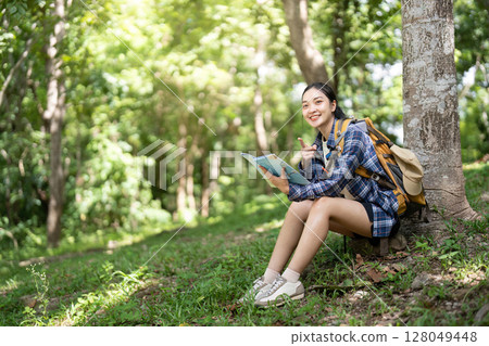 Joyful Hiking Experience. Young woman reading a map while resting in a forest. 128049448