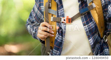 Nature Exploration. Woman fastening backpack straps in the forest. Nature Exploration. Woman fastening backpack straps in the forest. 128049450