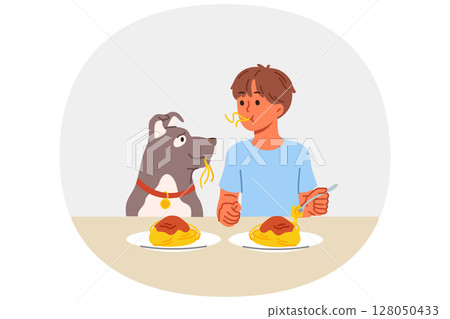 Little boy and dog eat spaghetti sitting at table, demonstrating friendship and trust 128050433