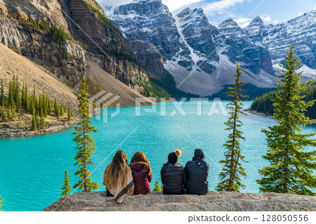 Four female tourists look out over the blue glacial lake and snowy mountains at Moraine Lake, Alberta, Canada. Four female tourists look out over the blue glacial lake and snowy mountains at Moraine Lake, Alberta, Canada. 128050556