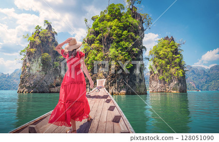 Panorama of the nature of famous places in Thailand - A woman in a Red dress looks at the landscape of mountains and rocks among the emerald waters of Cheo Lan Lake or sea in Khao Sok Park 128051090