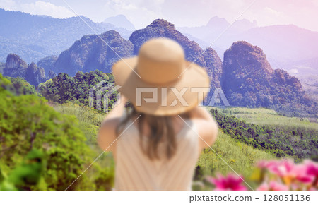 Beautiful view of Khao Sok Park in Thailand, its mountains and rainforest during the day. The figure of a female traveler photographer in a blur in the foreground at the viewing point. 128051136