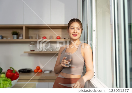 Refreshing Hydration. Woman enjoying a glass of water by the window. Refreshing Hydration. Woman enjoying a glass of water by the window. 128051277