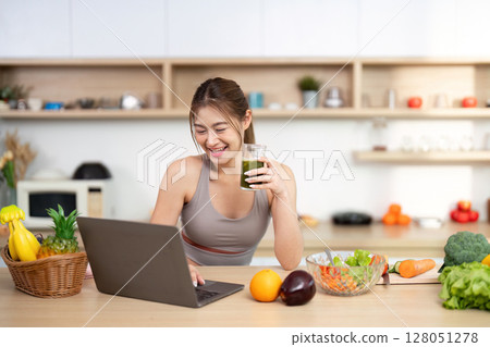 Healthy Living and Nutrition. Young woman smiling while sipping smoothie and using laptop. Healthy Living and Nutrition. Young woman smiling while sipping smoothie and using laptop. 128051278