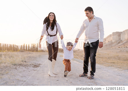 Family of three, a man, a woman and a child, are walking down a dirt road 128051811