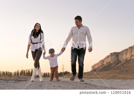Family of three, a man, a woman and a child, are walking down a dirt road Family of three, a man, a woman and a child, are walking down a dirt road 128051816