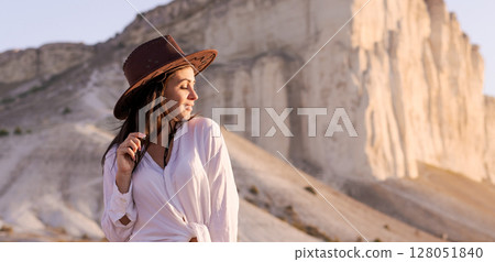 Woman wearing a brown hat and a white shirt is standing on a rocky hill 128051840