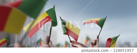 Benin flags in their hands on a blurred urban background Benin flags in their hands on a blurred urban background 128051957