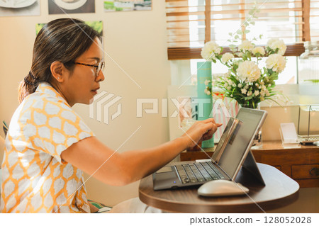 Asian woman working with a laptop sitting at a cafe table. Asian woman working with a laptop sitting at a cafe table. 128052028