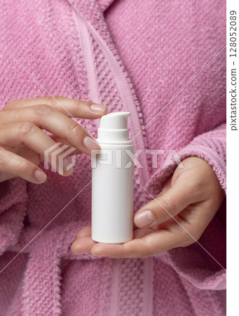 Closeup of woman in pink bathrobe holding white one pump cream tube in hands, cosmetic mockup Closeup of woman in pink bathrobe holding white one pump cream tube in hands, cosmetic mockup 128052089