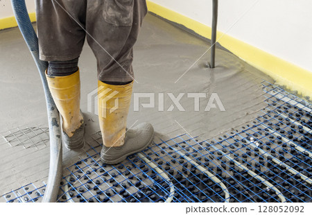 Man pouring concrete over floor heating installation in a new building. Modern construction system 128052092