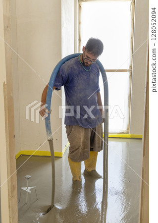 Worker wearing yellow rubber boots pouring concrete over floor in a new house construction site. Worker wearing yellow rubber boots pouring concrete over floor in a new house construction site. 128052094