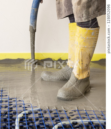 Man pouring concrete over floor heating installation in a new building. Modern construction system Man pouring concrete over floor heating installation in a new building. Modern construction system 128052096