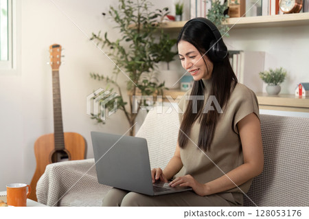 Remote Work and Focused Learning. Young woman using laptop with headphones. Remote Work and Focused Learning. Young woman using laptop with headphones. 128053176