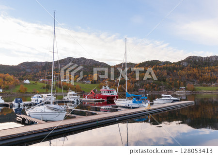 Serene view of a marina hosting sailboats and yachts and reflecting calm waters 128053413