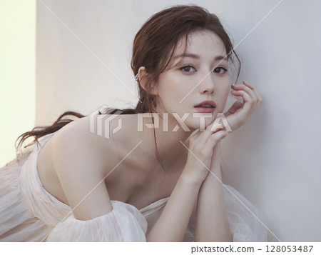 Woman is wearing a white dress and is leaning against a wall 128053487