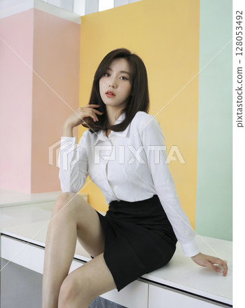 Woman is sitting on a table wearing a white shirt and black skirt Woman is sitting on a table wearing a white shirt and black skirt 128053492