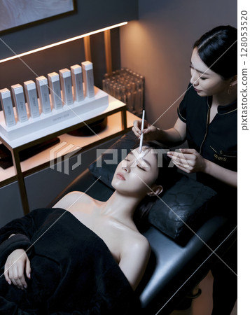 Woman is getting her face done by another woman Woman is getting her face done by another woman 128053520