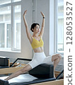 Woman in a yellow top and white shorts is doing a yoga pose on a black 128053527