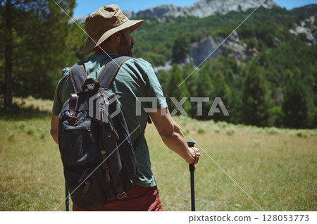 Man Hiking in Mountain Landscape with Backpack and Trekking Poles 128053773
