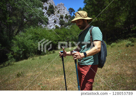 Man Hiking in Scenic Mountain Landscape Carrying Hiking Poles on a Sunny Day 128053789