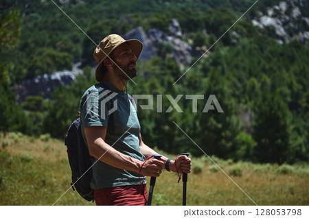 Man Hiking in a Mountain Forest on a Summer Day with Gear and Walking Sticks 128053798