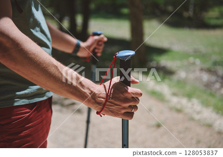 Young Man Hiking on a Trail Holding Trekking Poles in Summer Young Man Hiking on a Trail Holding Trekking Poles in Summer 128053837