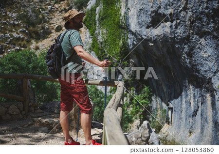 Man Hiking on a Scenic Mountain Trail with Backpack and Trekking Poles 128053860