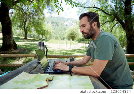 Remote Work Outdoors: A Man Uses a Laptop While Traveling in Nature Remote Work Outdoors: A Man Uses a Laptop While Traveling in Nature 128054534