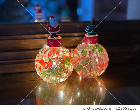 Glowing christmas ornaments with santa claus and a festive tree, reflecting on a wooden table 128055115