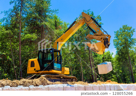 Heavy machinery is actively lifting large stone block during build retaining walls construction project 128055266
