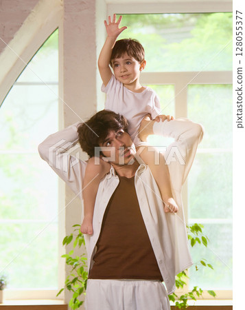 Everyday adventure. Father and son enjoying playful moment with child on dad's shoulders indoors 128055377