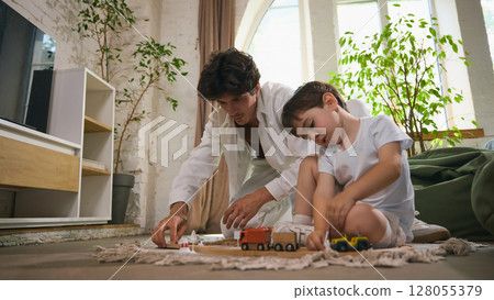 Father and son enjoying quality time playing with toy cars on living room floor 128055379