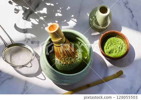 Traditional Matcha Preparation. Elegant matcha tea setup with a whisk, strainer, and green powder Traditional Matcha Preparation. Elegant matcha tea setup with a whisk, strainer, and green powder 128055503