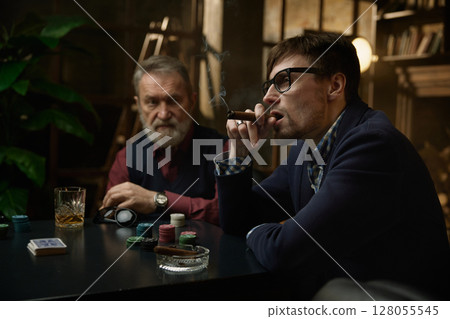 Three men enjoying tense poker game unfolds in a beautifully decorated vintage setting 128055545